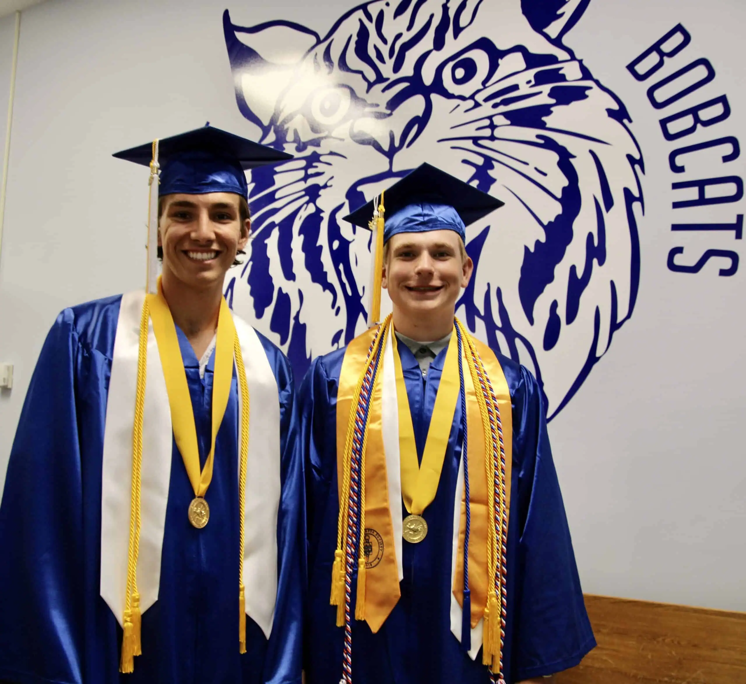 (Rick Miller/Olean Star) Hinsdale Valedictorian Tyler Richards (right) and Salutatorian Peyton Keller stand in front of a Bobcat mural at the school’s main entrance Friday night. Twenty-eight seniors graduated in the school auditorium.