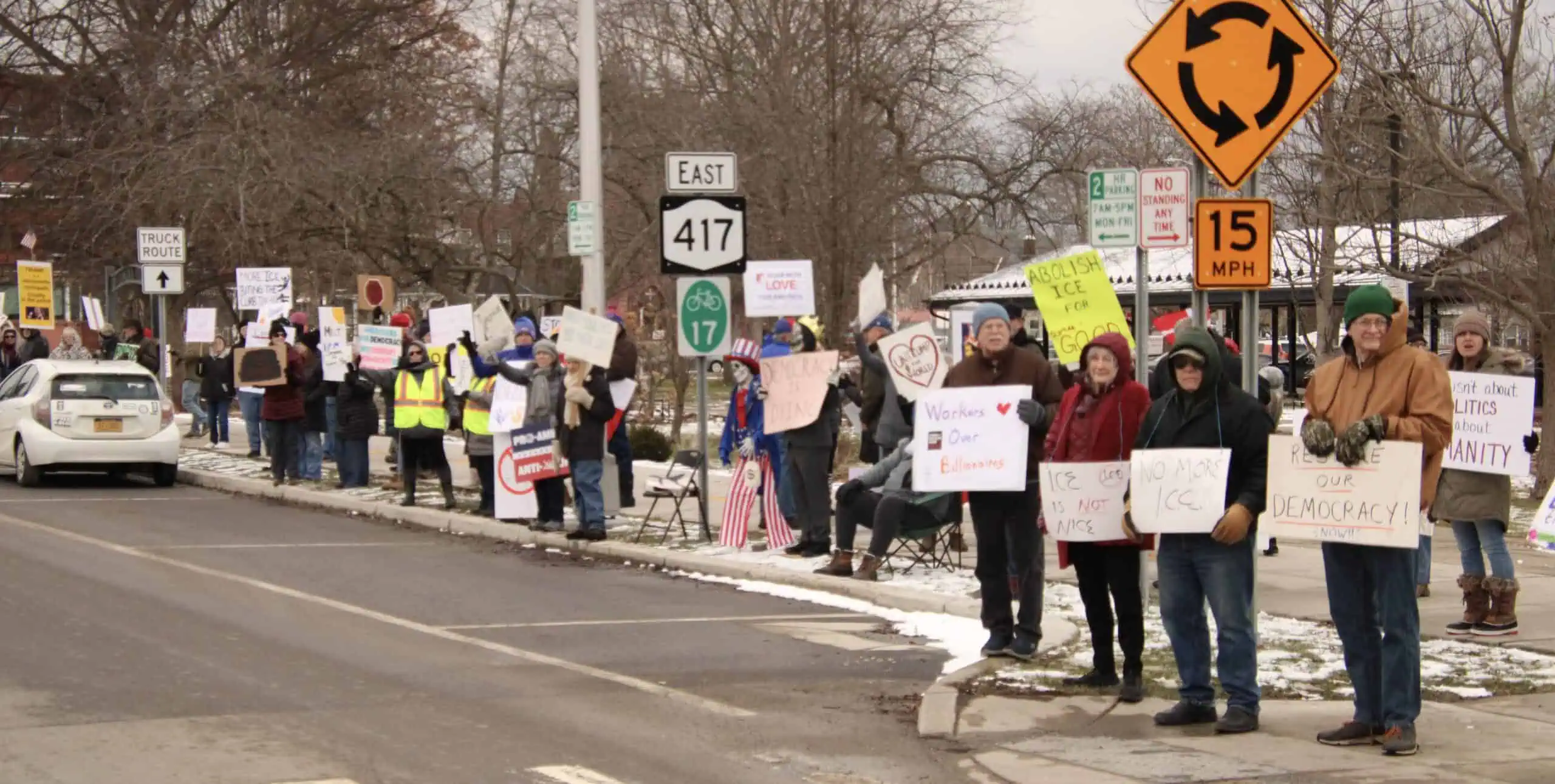 (Rick Miller/Olean Star) Protesters carrying signs demonstrate outside LIncoln Park in Olean on Saturday to mark the first year of President Trump's second term.